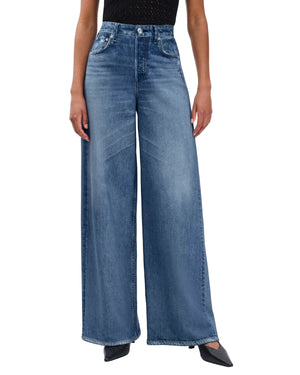 Person wearing Rag & Bone Miramar Sofie Ankle high-waisted, wide-leg blue jeans with a black sleeveless top, standing with arms relaxed and facing forward.
