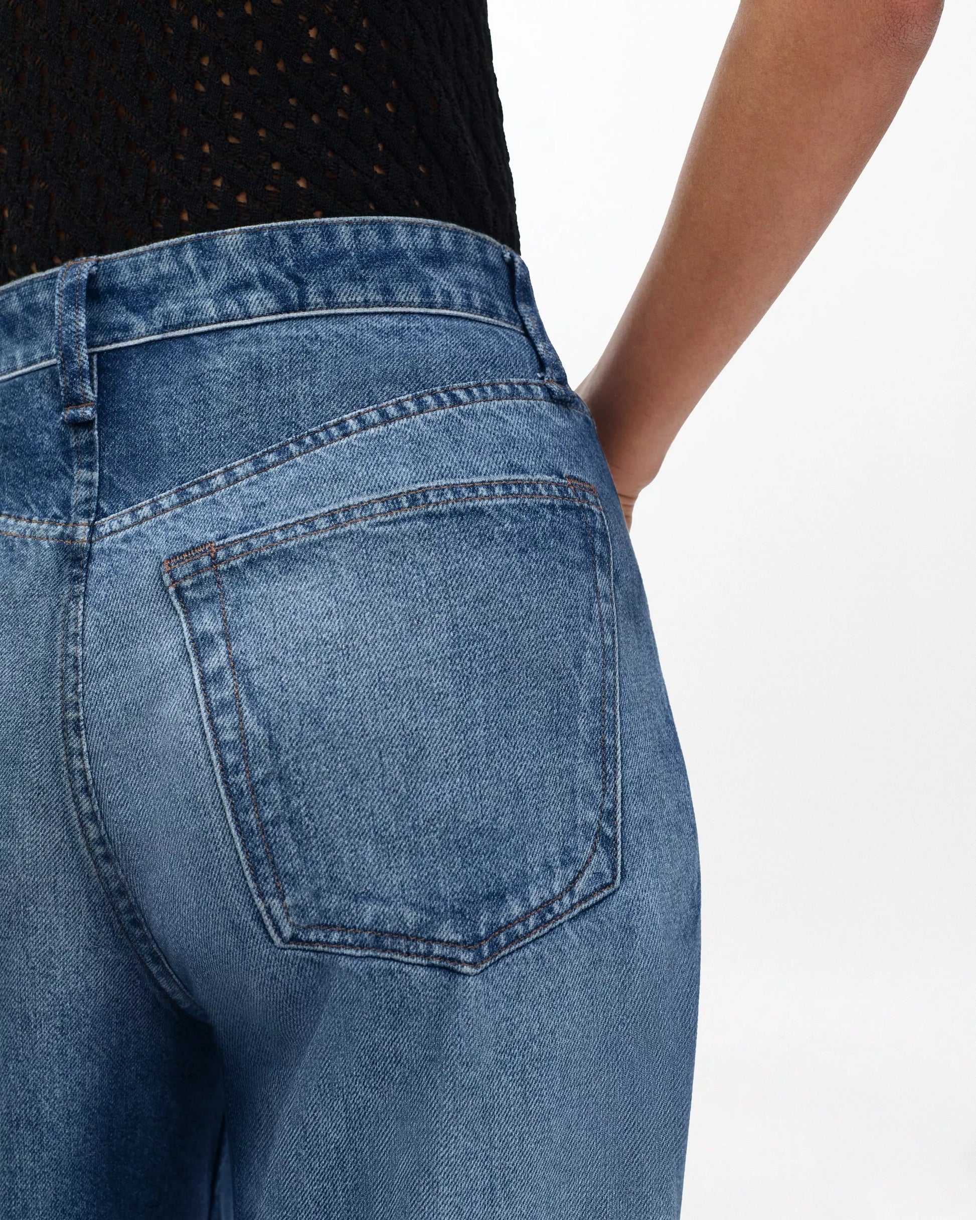 Person wearing Rag & Bone Miramar Sofie Ankle pants and a black textured top, shown from the back with one hand on their hip.