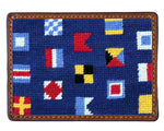 The Smathers & Branson Mixed Signals Card Wallet is a hand-stitched rectangular wallet with blue needlepoint fabric, colorful nautical signal flags, and rich brown leather trim.