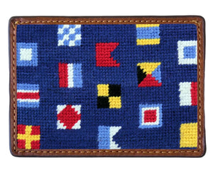 The Smathers & Branson Mixed Signals Card Wallet is a hand-stitched rectangular wallet with blue needlepoint fabric, colorful nautical signal flags, and rich brown leather trim.