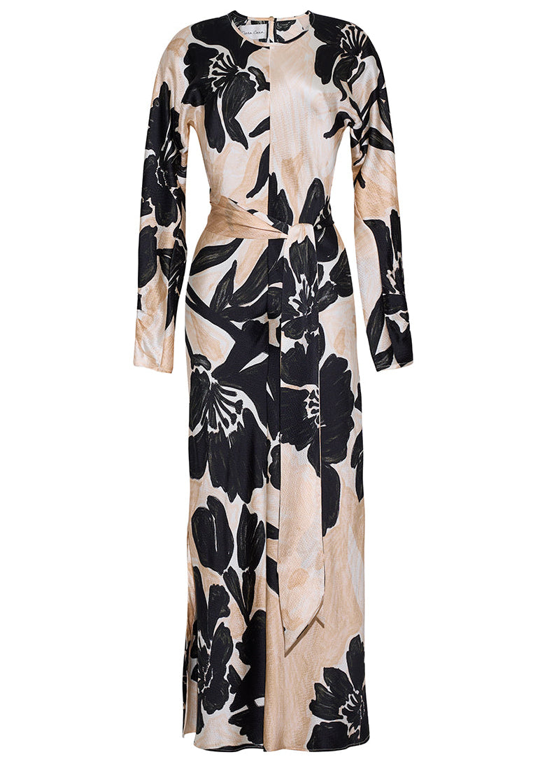 The Montgomery Silk Midi Dress by Cara Cara is a beige, long-sleeved hammered silk column dress with black oversized floral print and a front waist tie, shown against a white background.
