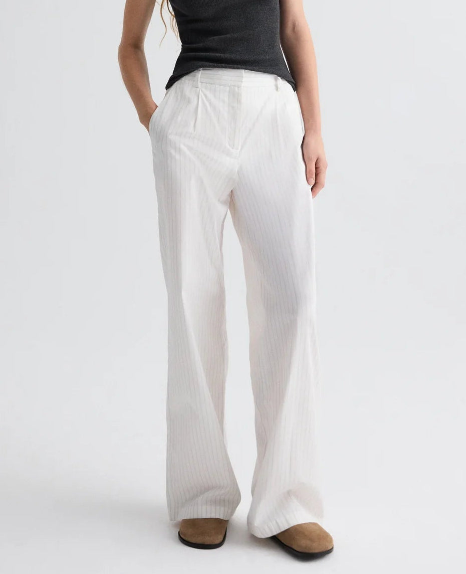 A person wearing a black sleeveless top, brown shoes, and TWP's Hudson St. Cotton Stripes Pant stands against a plain light background.