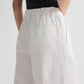 A person wears TWP’s Hudson St. Cotton Stripes Pant—a high-waisted, wide-leg white pinstripe cotton poplin trouser—paired with a sleeveless black top, shown from the waist down with hands behind their back.