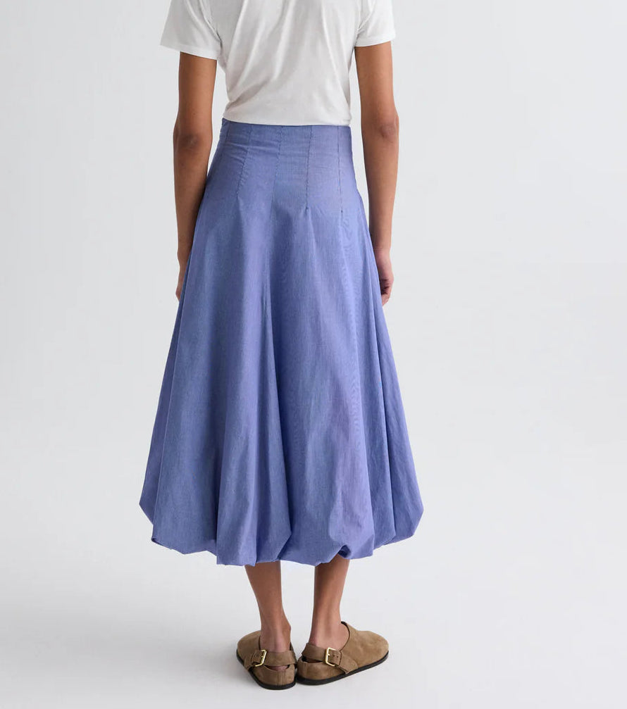 A person stands against a plain background wearing a white short-sleeve shirt, brown slip-on sandals, and the TWP Full Intentions Cotton Poplin Skirt in blue.