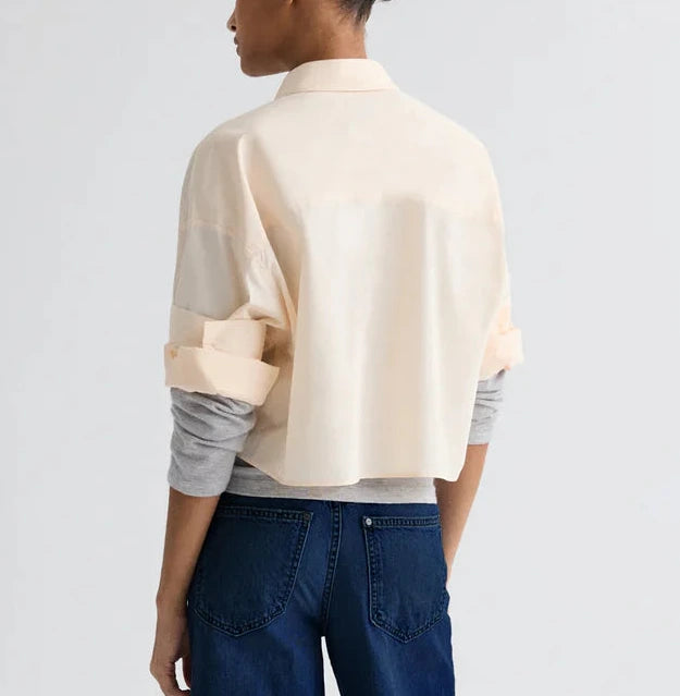 Person standing with their back to the camera, wearing the TWP Next Ex Superfine Cotton Shirt over a gray long-sleeve shirt and blue jeans.