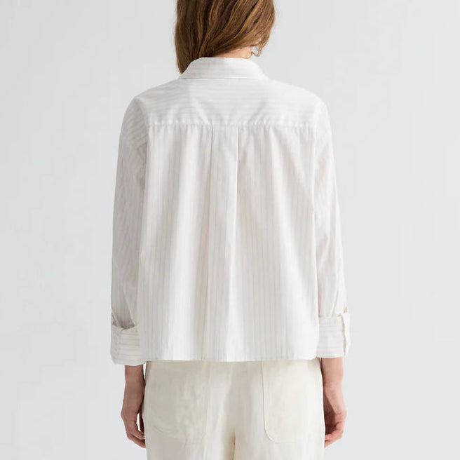 A person with long hair is seen from the back wearing the TWP J.D. Striped Shirt and light pants, set against a plain background.