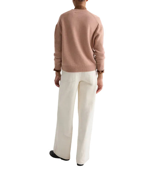 A person stands with their back to the camera, wearing the TWP Boy Cashmere Crew sweater in light brown, white wide-leg pants, and black shoes against a white background.