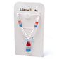 The Popsicle Rocket Red White Blue Necklace by Lillies & Roses features red, white, and blue beads with a rocket popsicle pendant, presented on a branded card.