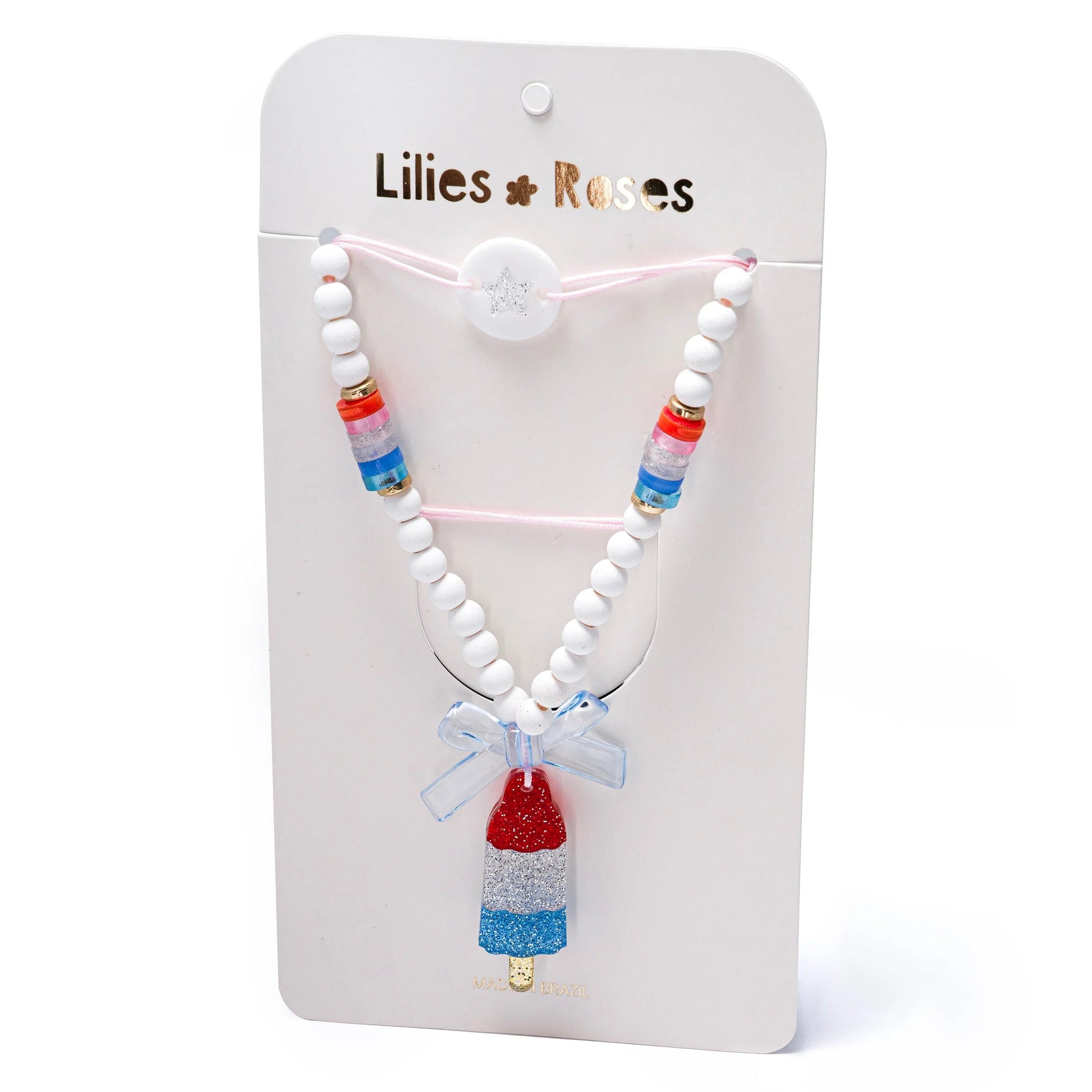The Popsicle Rocket Red White Blue Necklace by Lillies & Roses features red, white, and blue beads with a rocket popsicle pendant, presented on a branded card.