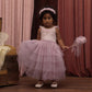 A young girl wears the Noralee Girls’ Pixie Dress, featuring a velvet bodice and tulle skirt, as she stands on a wooden floor holding a matching wand, with pink curtains in the background.