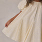 A child wearing the Noralee Baby Girls’ and Girls’ Maia Dress in off-white, featuring short sleeves and embroidered heart eyelet details, holding the skirt out to the side.