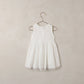 The Noralee Girls’ Georgia Dress is a sleeveless white baby mini dress featuring decorative buttons, delicate eyelet detailing, and lace trim, shown hanging on a metal hanger against a simple light background—perfect for special occasions.