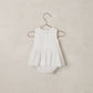 The Noralee Baby Girls’ Georgia Romper features a white sleeveless design with a scalloped neckline, ruffled collar, eyelet lace skirt detail, and button front for easy changing, displayed on a hanger against a neutral background.