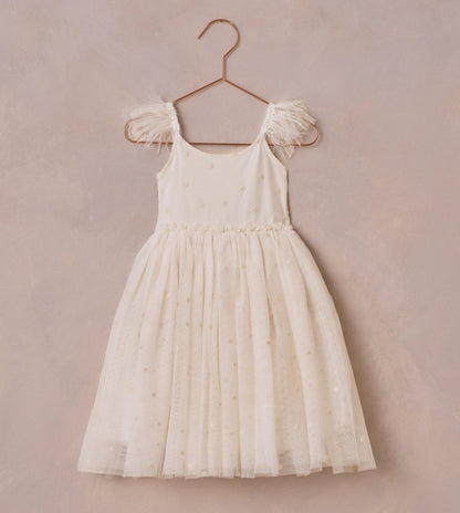 The Girls' Poppy Dress by Noralee is an elegant ivory dress with a tulle skirt and feathered shoulder straps, beautifully adorned with floral embroidery. It hangs gracefully on a rose gold hanger against a textured beige background.