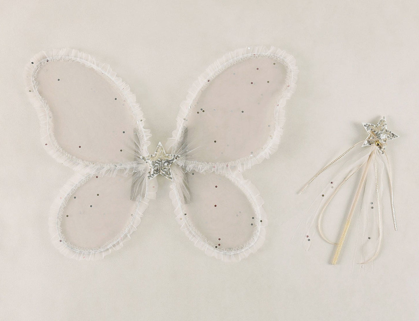 Sheer white butterfly wings adorned with glitter accents are displayed beside a coordinating star-shaped wand decorated with silver ribbons, both included in the Girls’ Fairy Set by Noralee, set against a simple light backdrop.