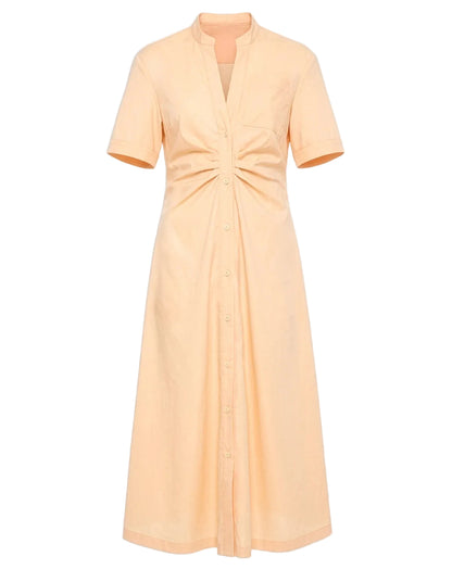 The Noor Dress by Callas Milano is a peach fit and flare midi shirt dress featuring short sleeves, a v-neck, button-down front, and ruched waist detail for a flattering silhouette.