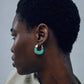 A person with short, curly hair is shown in profile wearing Lizzie Fortunato Organic Mini Gold Hoops. The background is plain and neutral.