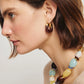A woman with short brown hair wears a chunky beaded necklace in blue, yellow, and brown by Lizzie Fortunato, paired with Lizzie Fortunato's Organic Mini Gold Hoops.