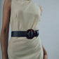 A person in a sleeveless beige dress wears the Lizzie Fortunato Louise Tortoise Acrylic Buckle Belt featuring an oversized tortoiseshell buckle.