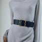 A person in a light gray dress cinched with the wide Lizzie Fortunato Florence Gold Buckle Belt featuring an ornate gold-plated buckle.