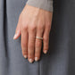 A hand with short, natural nails wears the Nanna Ring by Lie Studio, a classic curved sterling silver band, on the ring finger against a gray fabric background.
