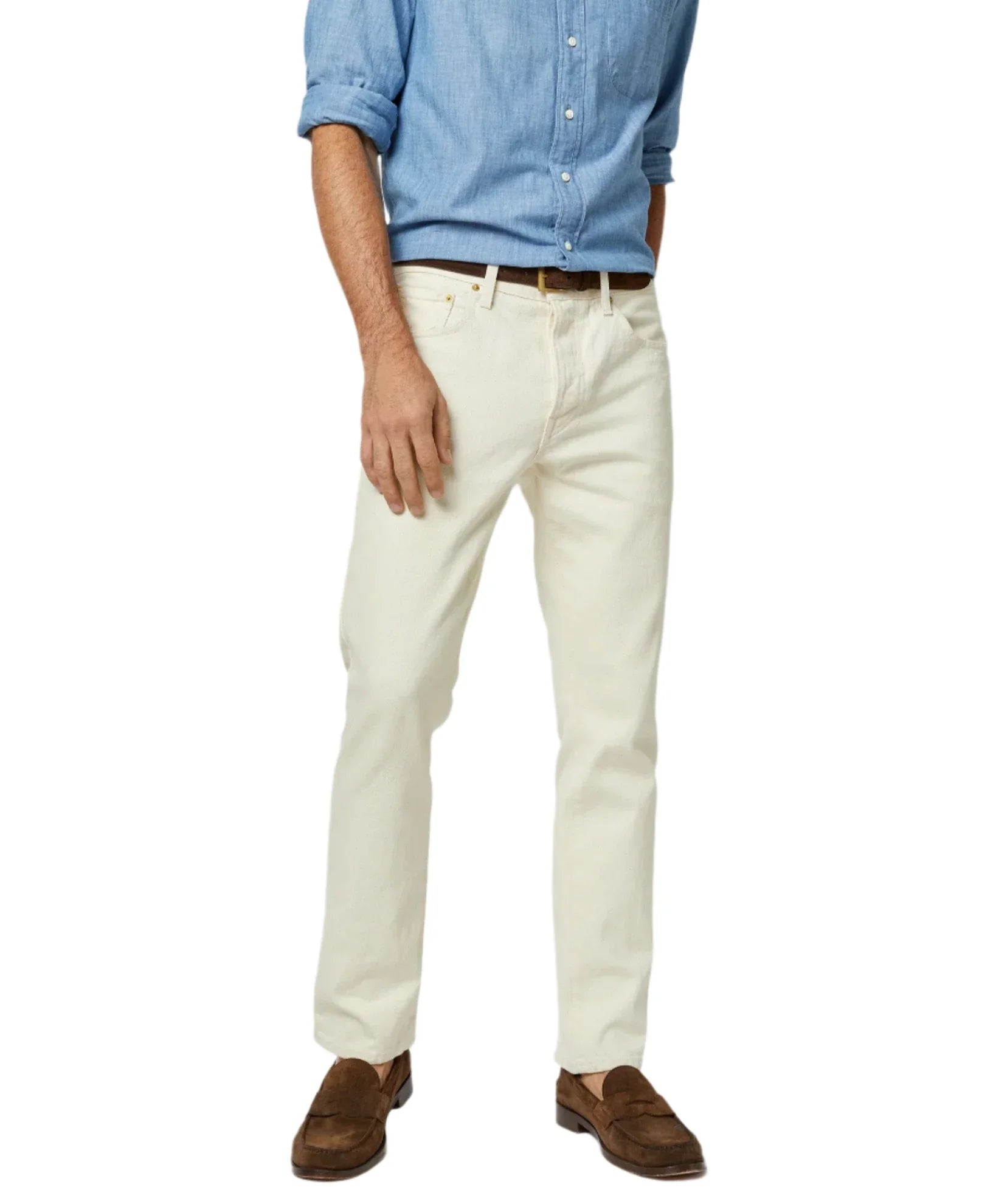 A person wearing a light blue shirt, cream-colored pants, and brown loafers stands against a white background, showcasing a classic style often complemented by Sid Mashburn's Slim Straight Jean, crafted in the USA.