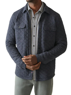 A person wearing the Faherty Epic Quilted Fleece in navy over a relaxed-fit shirt and gray pants stands against a plain background.