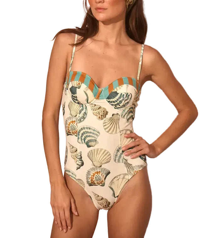 A woman wears the Nevis One Piece by Hunter Bell NYC, a flattering swimsuit with a shell and sea-inspired print, thin straps, and striped trim along the top.