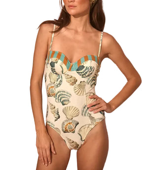 A woman wears the Nevis One Piece by Hunter Bell NYC, a flattering swimsuit with a shell and sea-inspired print, thin straps, and striped trim along the top.