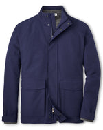 The Peter Millar Newport City Coat is a navy blue coat featuring a stand-up collar, zipper, and snap buttons. Designed to be water-resistant and windproof, it includes ribbed cuffs and two front pockets for enhanced functionality.