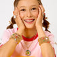 A young person in a pink shirt smiles, wearing colorful Super Stack Bracelet Set by Super Smalls—mix-and-match bracelets that are perfect everyday accessories.