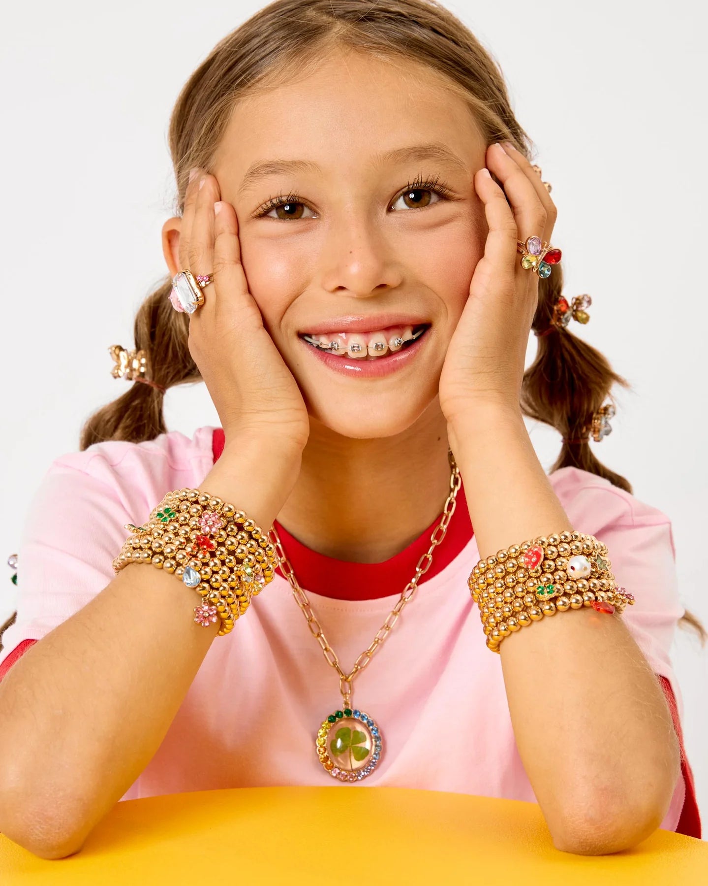 A young person in a pink shirt smiles, wearing colorful Super Stack Bracelet Set by Super Smalls—mix-and-match bracelets that are perfect everyday accessories.