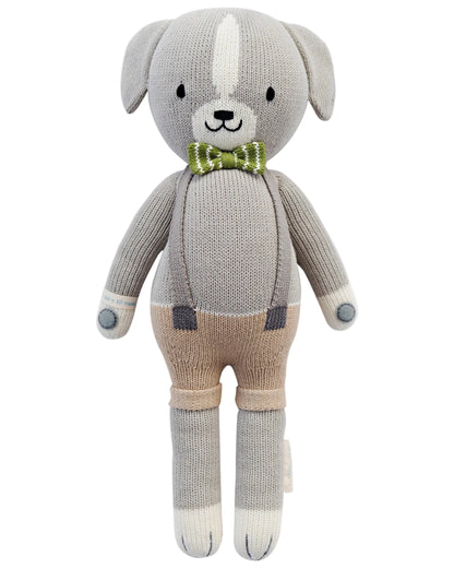 Noah the Dog - Little 13" by Cuddle + Kind is a knitted stuffed animal with a gray and beige body, white accents, green plaid bow tie, and suspenders—perfect as a cuddly plush toy for kids.