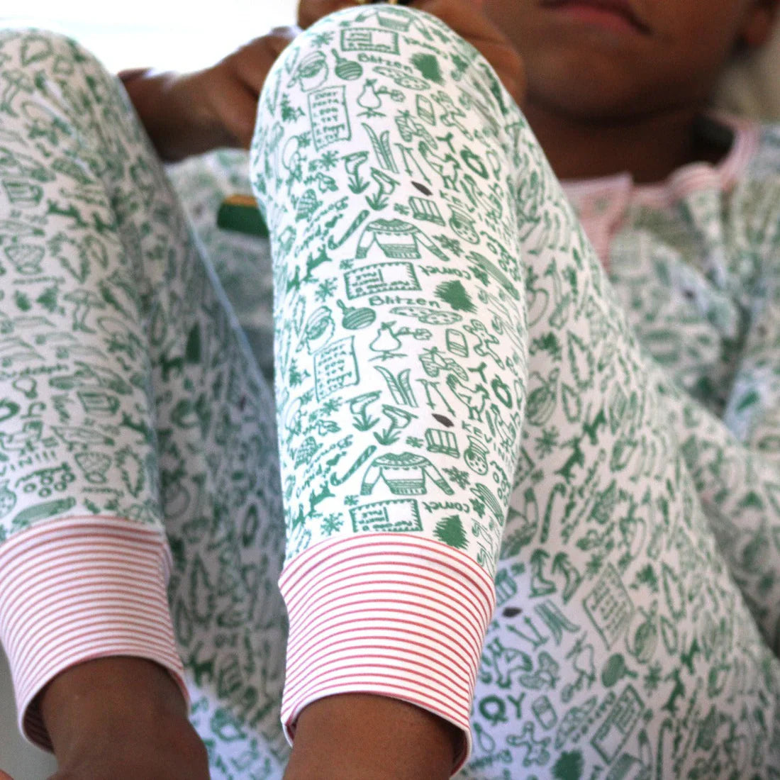 A close-up of someone wearing the Joy Street Kids North Pole Two Piece Henley Pajamas, featuring a white and green pattern with pink-striped cuffs, evoking the nostalgia of Christmas, while sitting with knees raised.