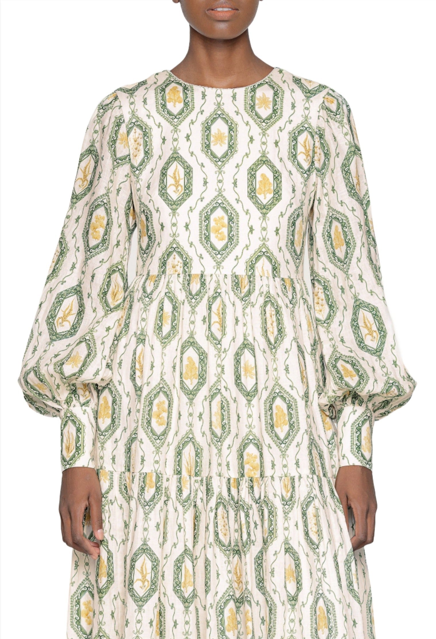 Woman wearing a long-sleeved Agua by Aguabendita Nuez Maxi Dress with a white and green geometric pattern, standing against a plain background.