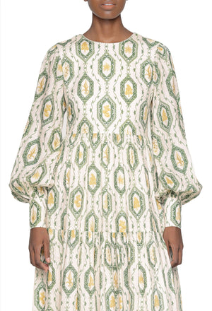 Woman wearing a long-sleeved Agua by Aguabendita Nuez Maxi Dress with a white and green geometric pattern, standing against a plain background.