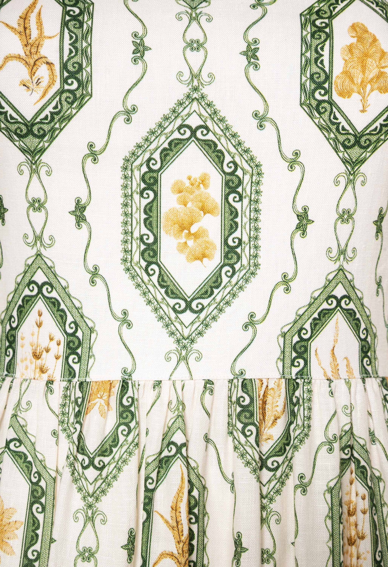 A close-up of an Agua by Aguabendita Nuez Maxi Dress with an intricate pattern featuring green and gold embroidered designs, including floral and vine motifs.