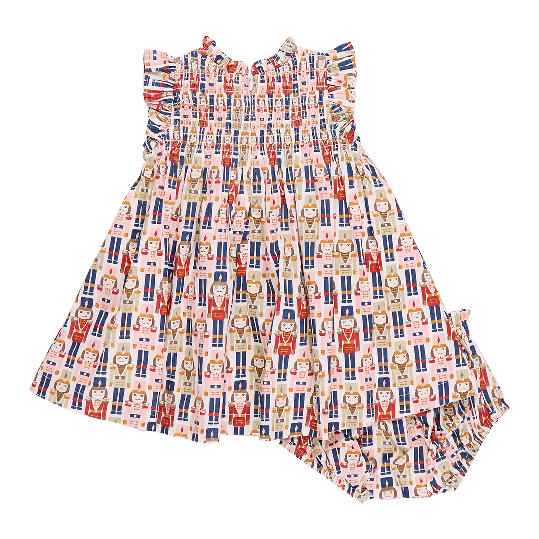 The Pink Chicken Baby Girls Stevie Dress, by Pink Chicken, is a charming children's dress and diaper cover set adorned with a colorful pattern of toy soldier illustrations on a white background.