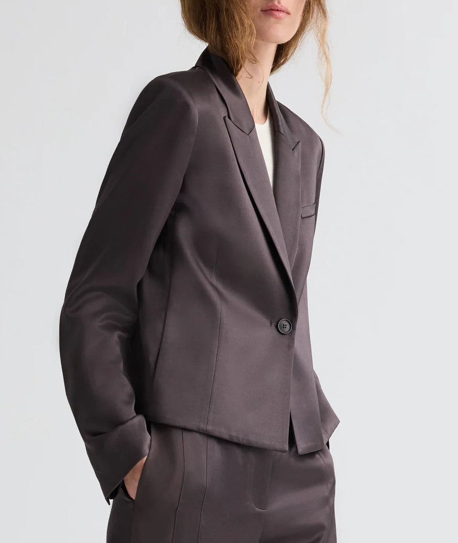 A person models the TWP Sawyer Shiny Viscose Wool Satin Blazer, styled with matching pants and hands in pockets, standing against a plain light background.