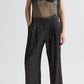 A person wears the TWP Sulli Sequin Netting Pant with a black bralette under a sleeveless, sheer metallic top and sandals.