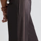 A person wearing TWP's Taite Shiny Viscose Wool Satin Pant in dark brown with high rise, wide leg, and side pocket, paired with a white shirt, shown from the waist down in a side view.