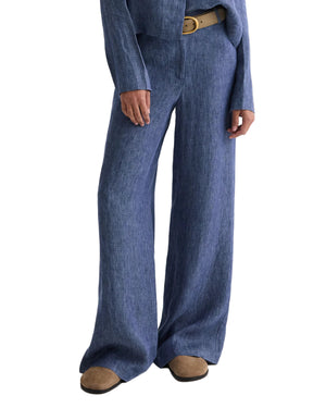 A person wears TWP’s Dylan Hemp Denim Pant in blue with brown shoes and a tan belt; the photo crops out the top half of their body.