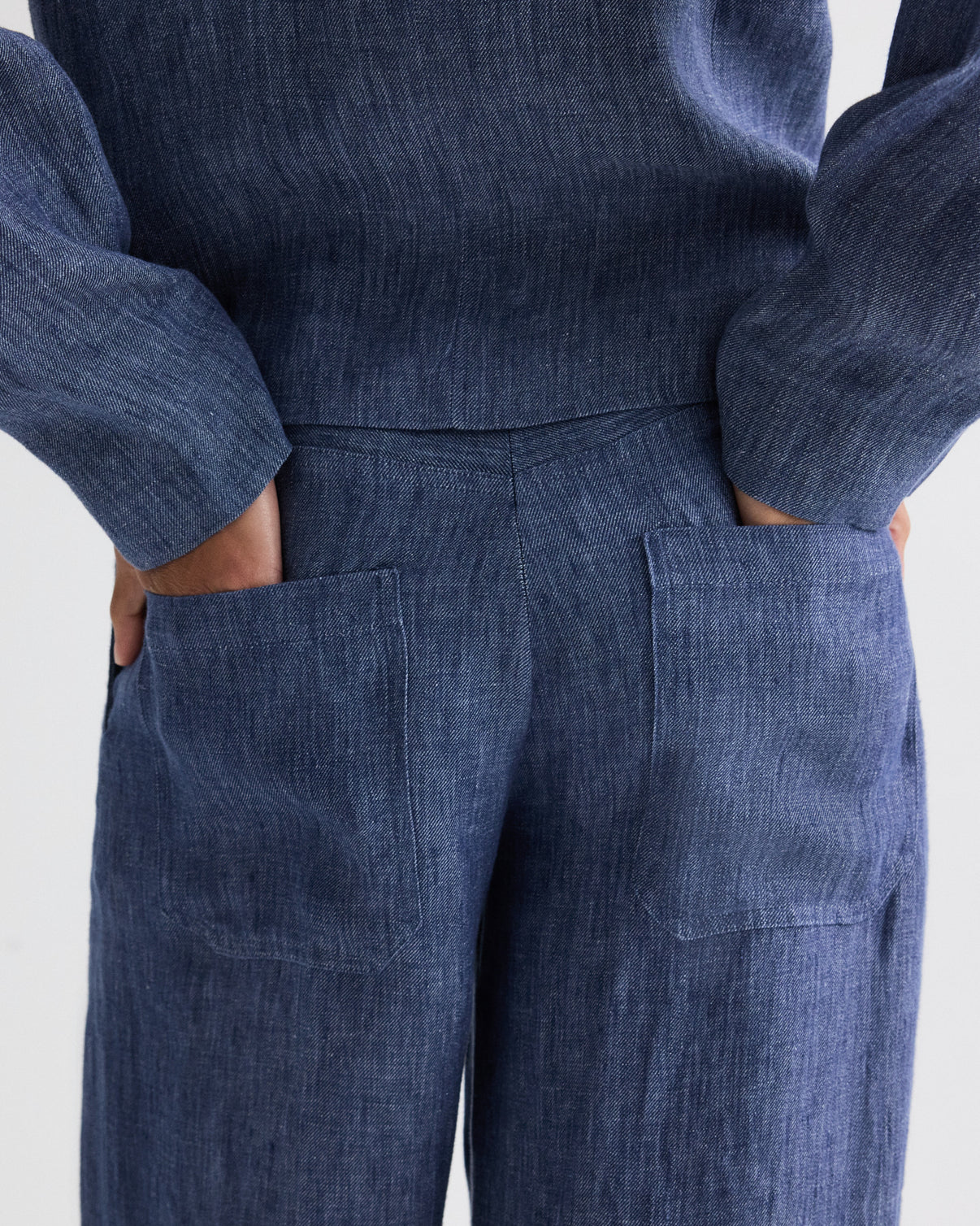 Model wears the TWP Dylan Hemp Denim Pant, shown from the waist down with hands in the back pockets of these blue textured high-rise trousers.