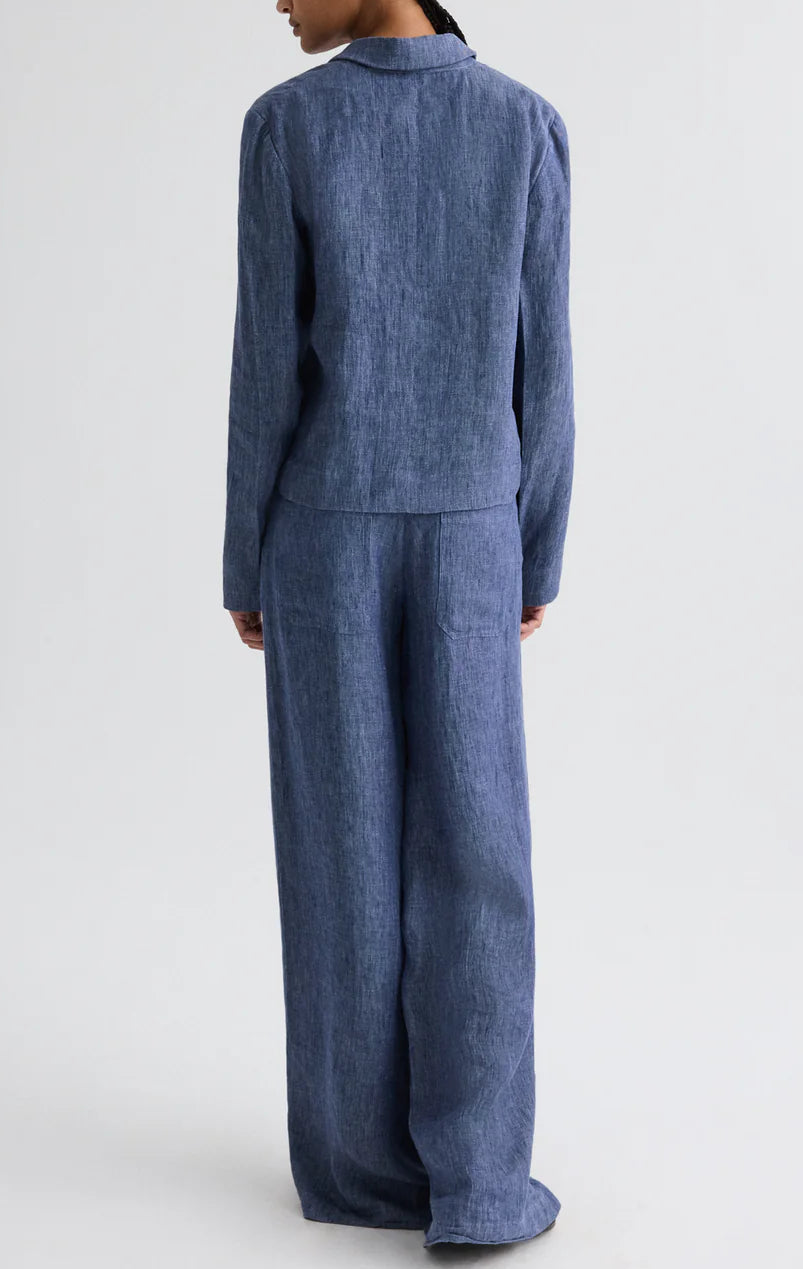 A person stands with their back to the camera, wearing TWP’s Dylan Hemp Denim Pant with a loose-fitting blue textured long-sleeve top, creating a relaxed yet stylish look.