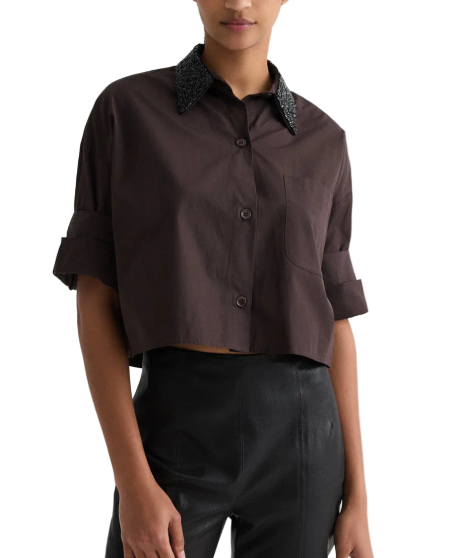 A woman wears the TWP Next Ex Crystal Collar Shirt—a cropped, dark brown Italian cotton button-up with a textured black collar—paired with high-waisted black pants.