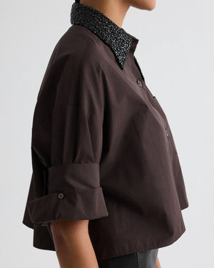 A person wears the TWP Next Ex Crystal Collar Shirt, a dark brown Italian cotton short-sleeve button-down with rolled cuffs and a textured black collar, shown in side view against a plain background.