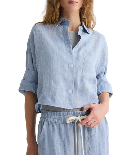 A person wears the TWP Next Ex Delave Hemp Shirt in light blue, cropped with rolled sleeves, paired with matching drawstring pants and a light gray top, creating a relaxed, boxy look.