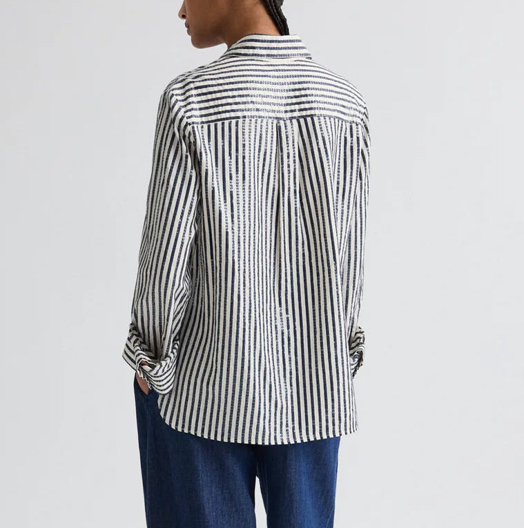 Model wearing the TWP Next Morning Clear Sequin Stripe Shirt in oversized Italian cotton with black-and-white vertical stripes, paired with blue pants, shown from the back against a plain light background.