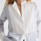 A woman wears TWP's The Night Before Cotton Stripes Shirt, featuring a pleated white bib front, pintuck details, a mandarin collar, and long sleeves; her hand rests in her pocket.