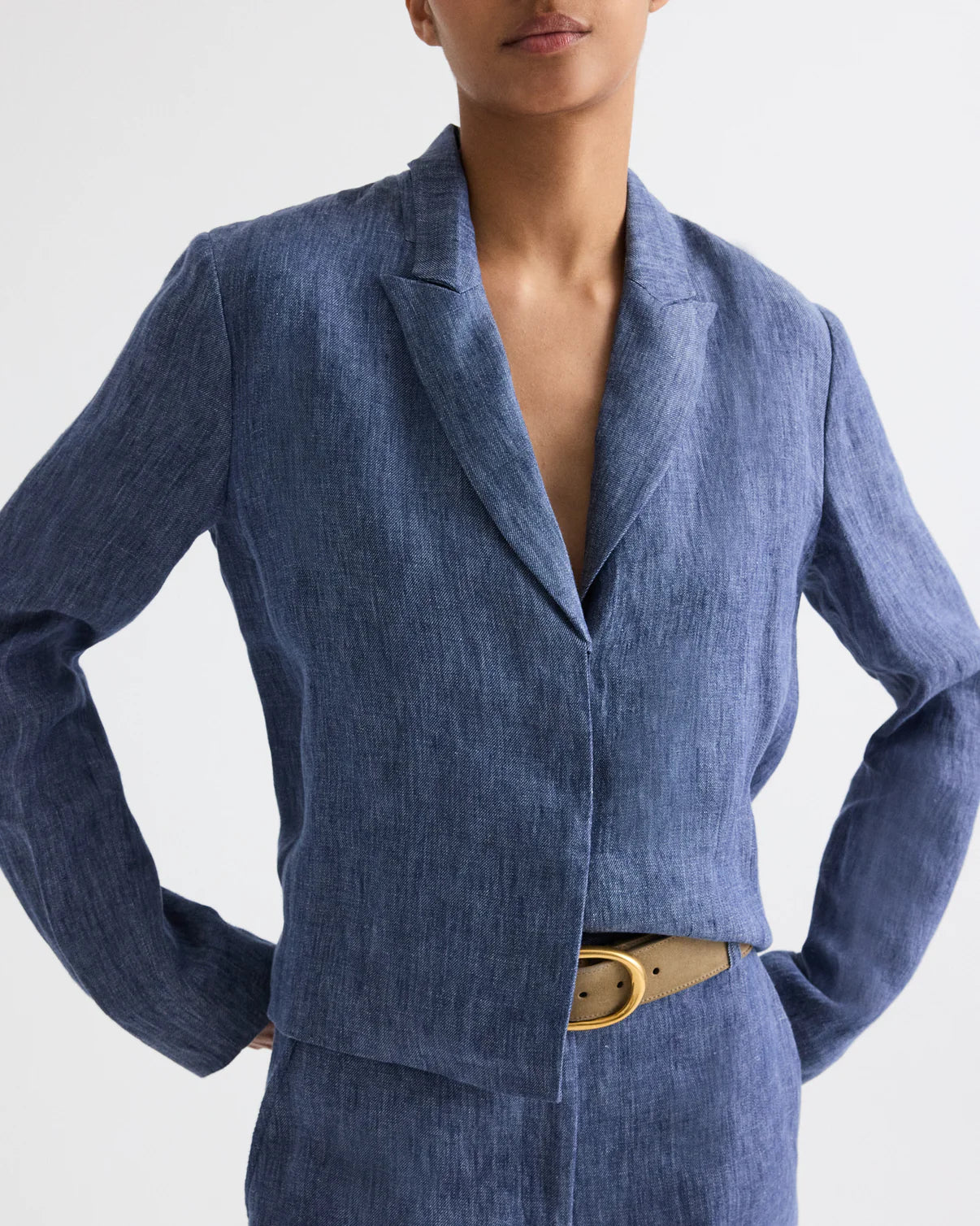 A person wearing the TWP Lucy Hemp Denim Top in blue, styled with matching pants and a beige belt, stands hands on hips against a plain background.